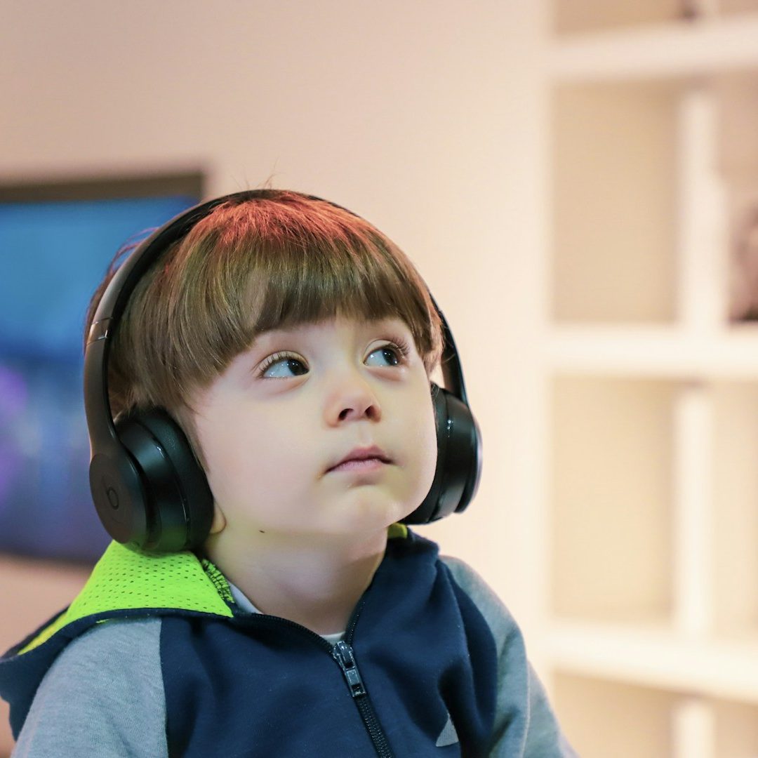 Child wearing black headphones, looking thoughtfully upwards.